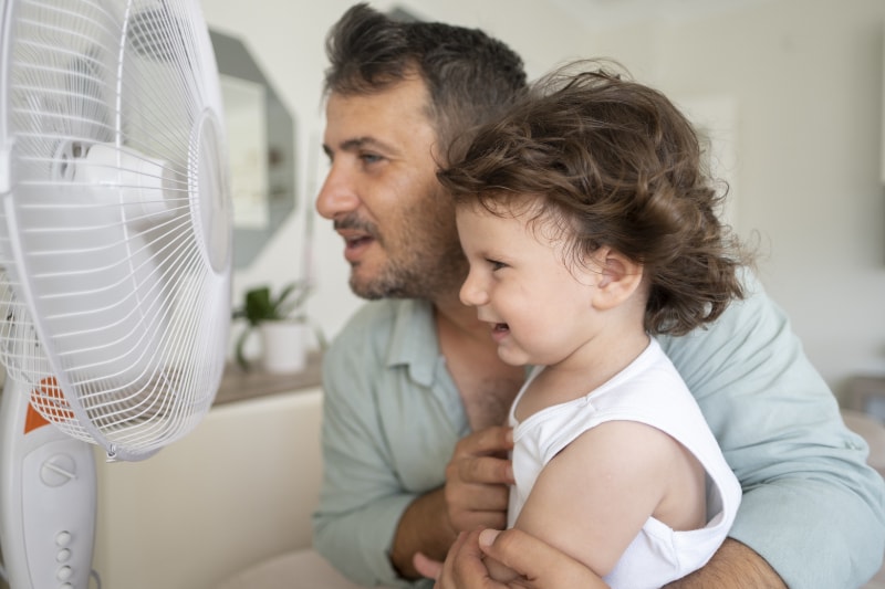 Father child is front of electric fan on hot summer day